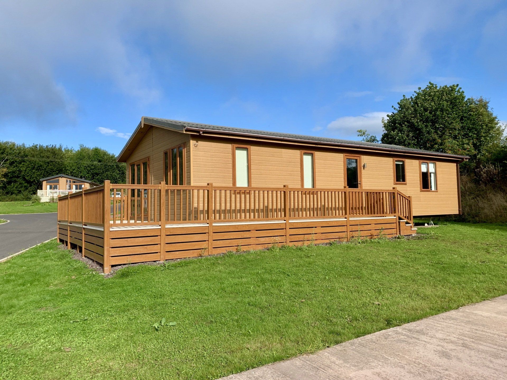 A mobile home with a large deck is sitting on top of a lush green field.