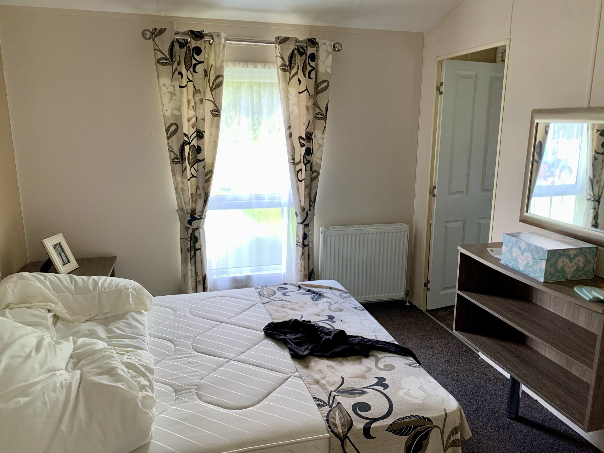 A bedroom with a bed , dresser , mirror and window.