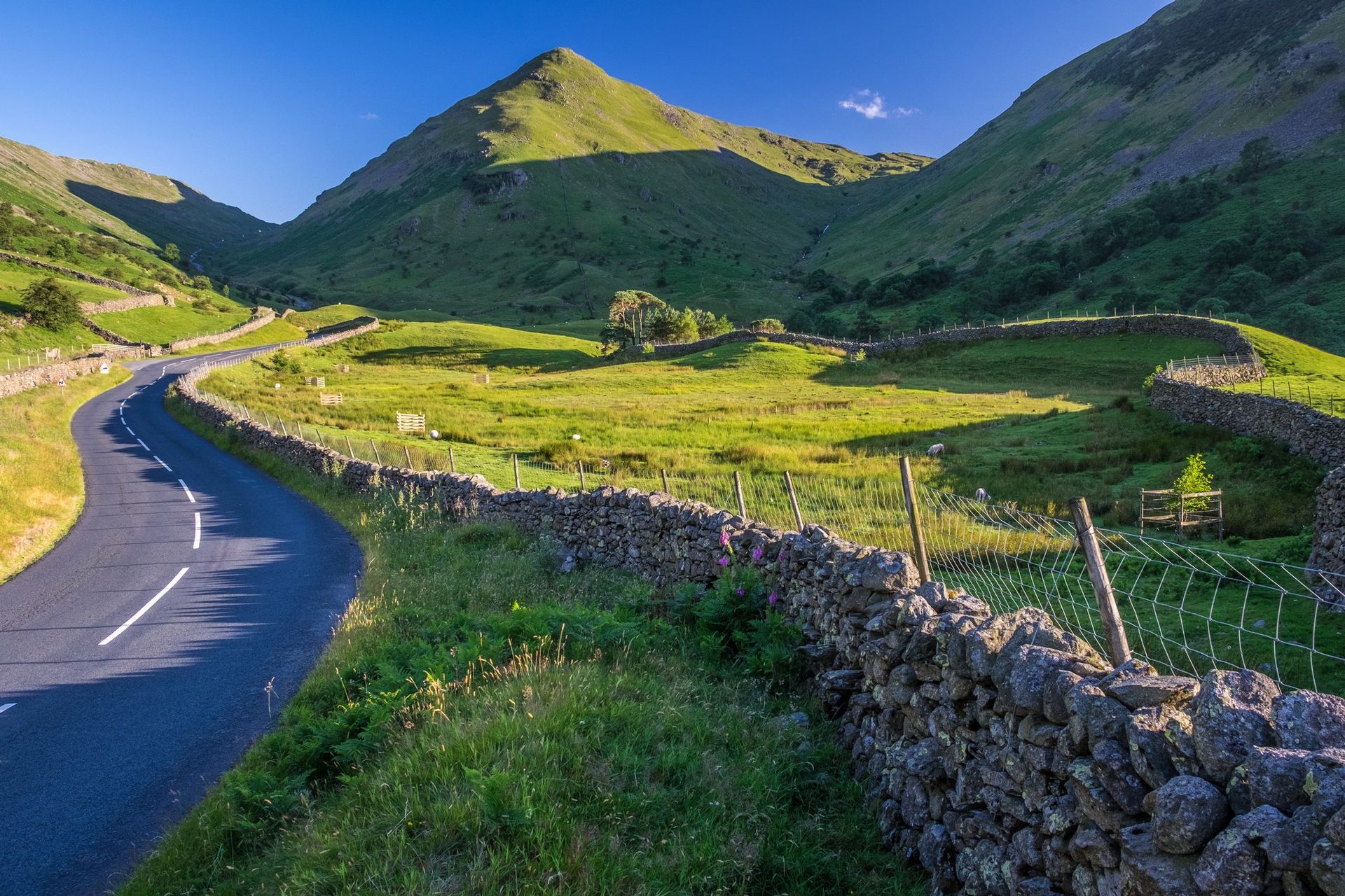 A road in the mountains with a stone wall and a mountain in the background.