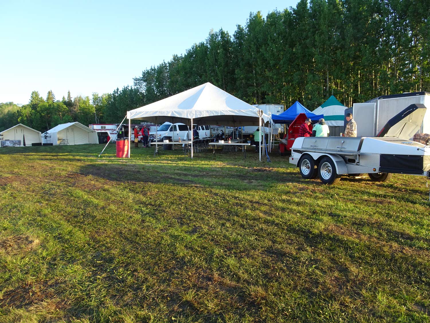 A trailer is parked in a grassy field with tents in the background