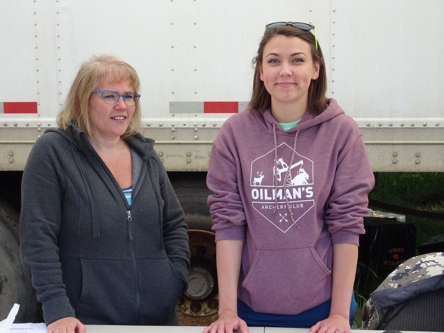 Two women are standing next to each other in front of a white trailer.