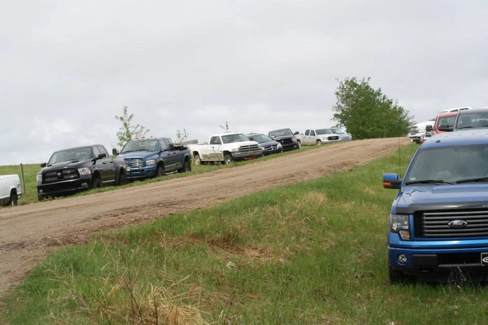 A row of trucks are parked on the side of a dirt road.
