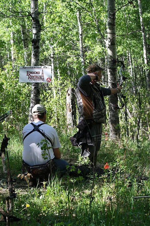 Two men are sitting in the woods with bows and arrows.