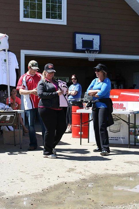 A group of people standing in front of a garage with a basketball hoop in the background.