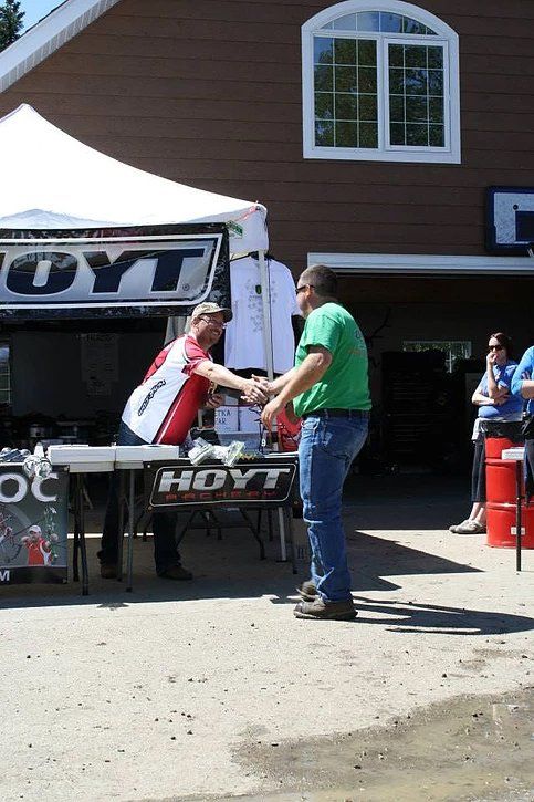 Two men shaking hands in front of a hayt tent