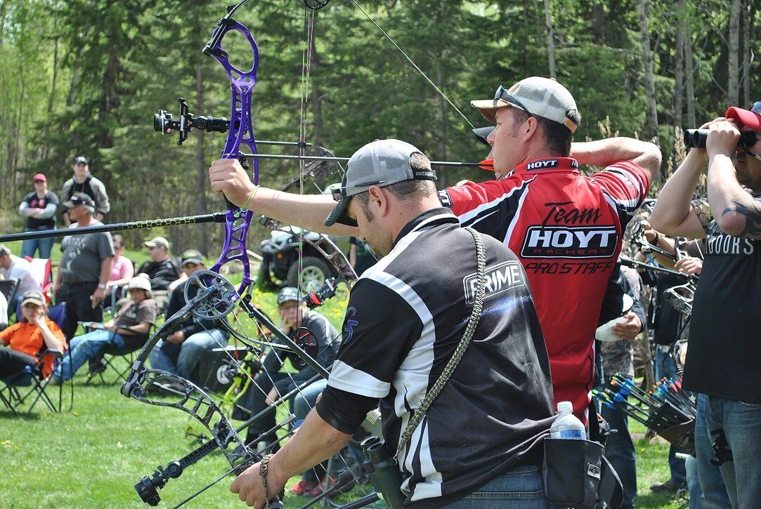 A group of men are standing in a field holding bows and arrows.