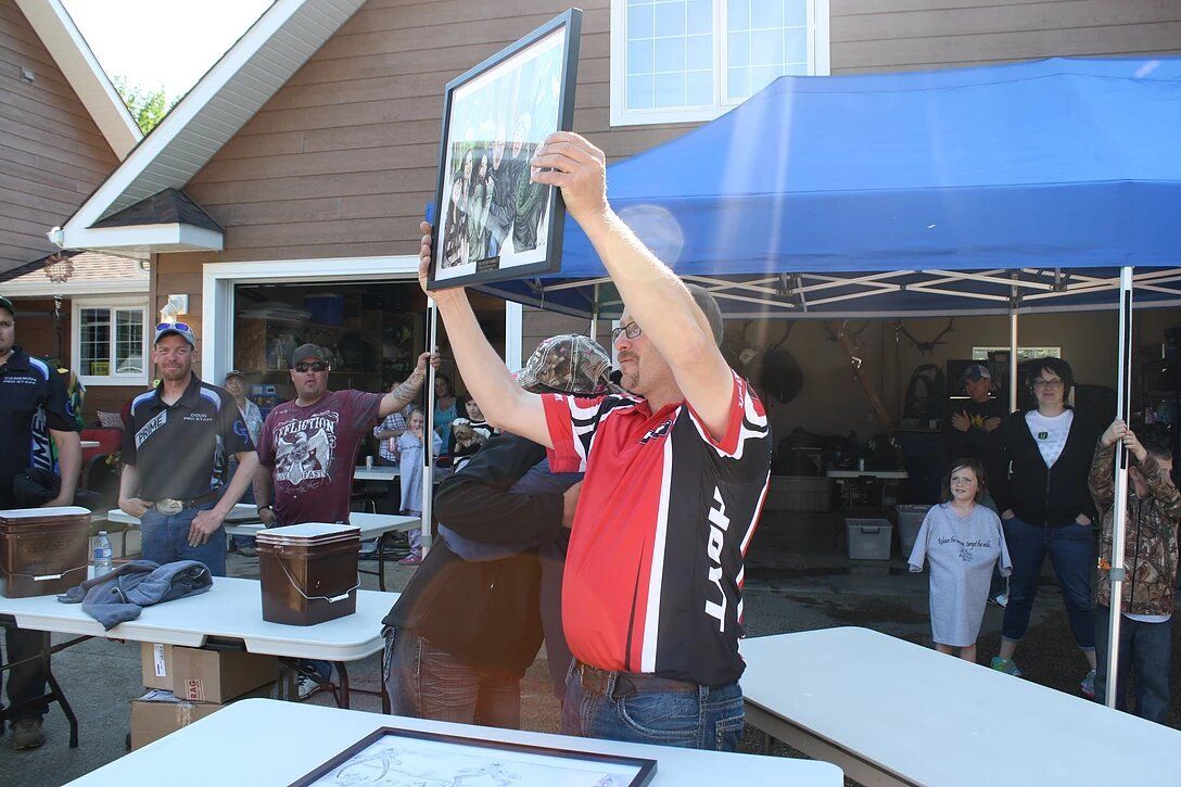 A man in a red and black shirt is holding up two framed pictures.