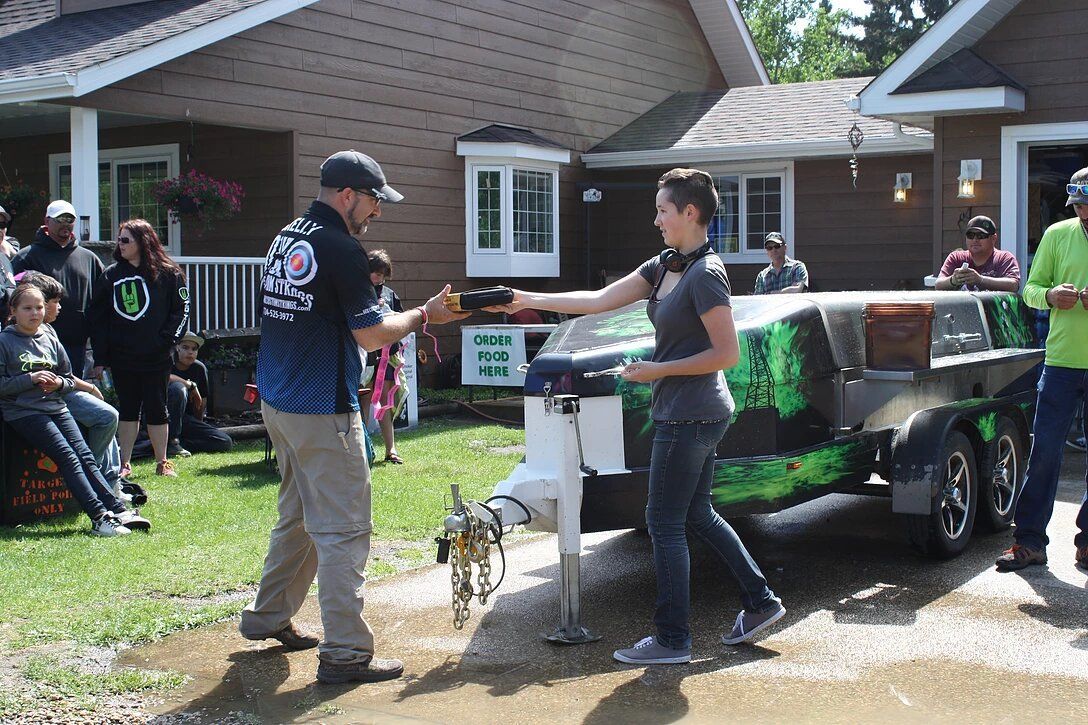 A man is handing a trophy to a woman in front of a house.