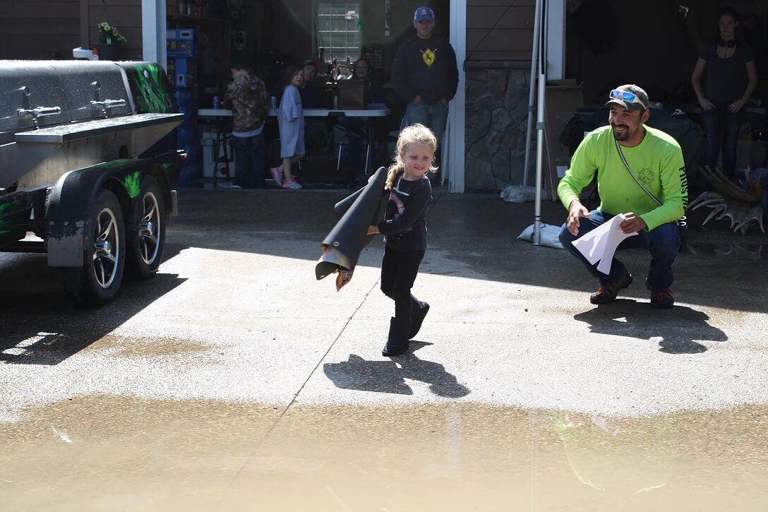 A little girl is jumping in a puddle while a man watches.