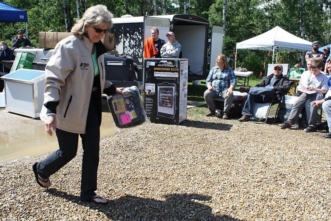 A woman is walking in a gravel area holding a box.
