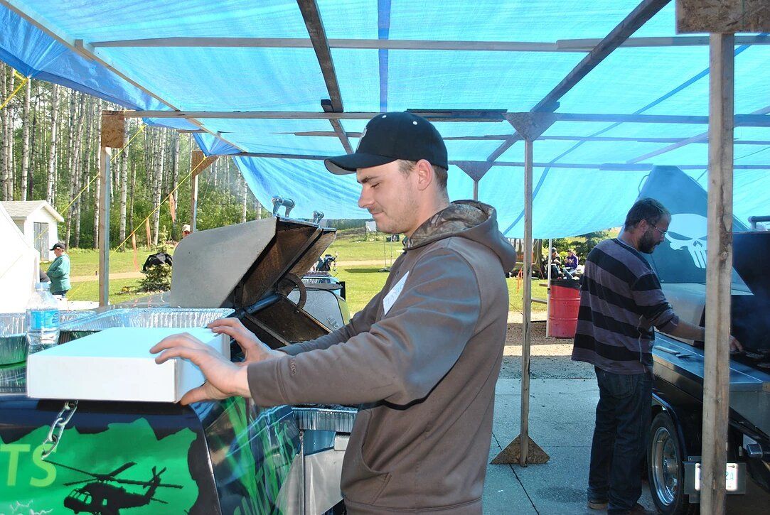 A man is standing under a blue tarp holding a box