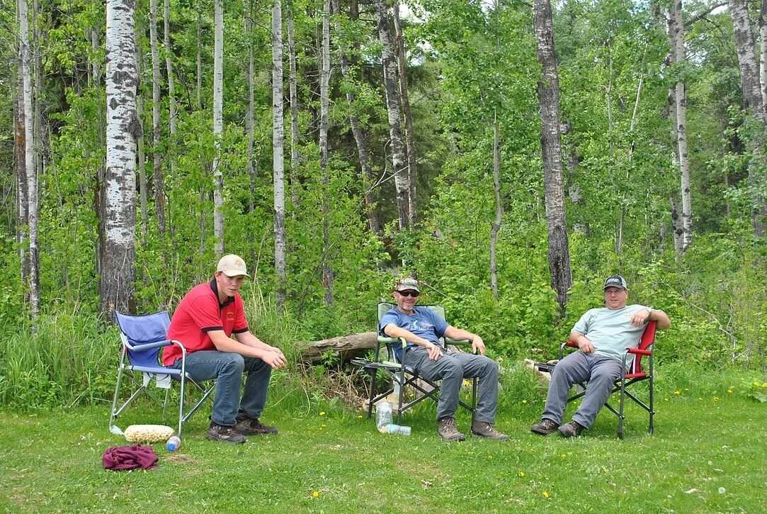 Three men are sitting in chairs in a field.