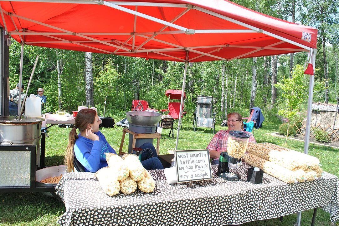 A woman is sitting at a table under a red tent selling potato chips.