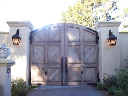 Large wooden double gate with stone pillars and wall lanterns at an entrance