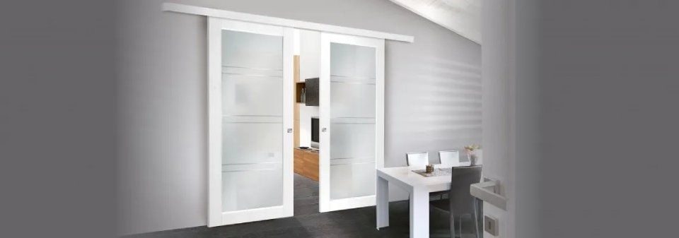 Doppie porte bianche in una stanza con soffitto inclinato, con una piccola scrivania e una sedia accanto.