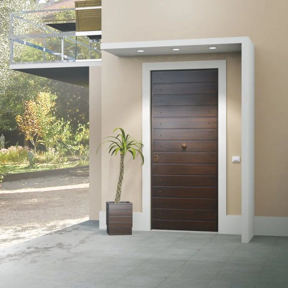 Ingresso di un'abitazione moderna con porta in legno scuro, parete beige, pianta in vaso e balcone sovrastante.