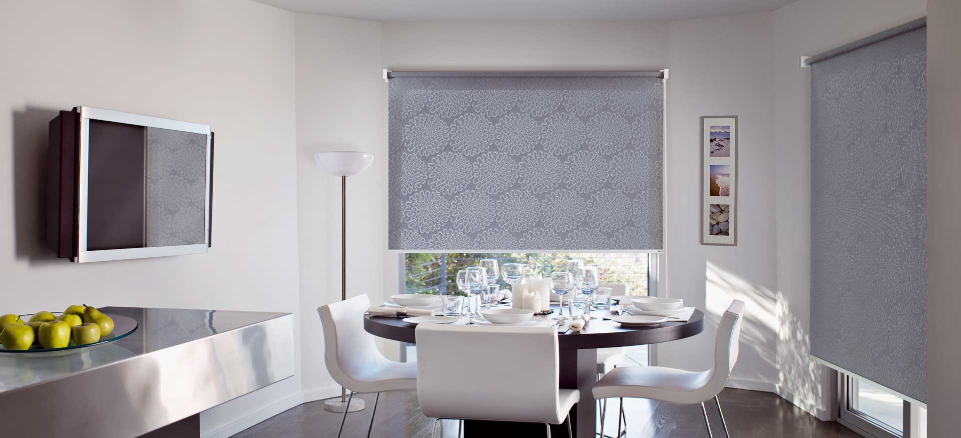 Sala da pranzo moderna con sedie bianche, tavolo rotondo e tende a rullo decorate.