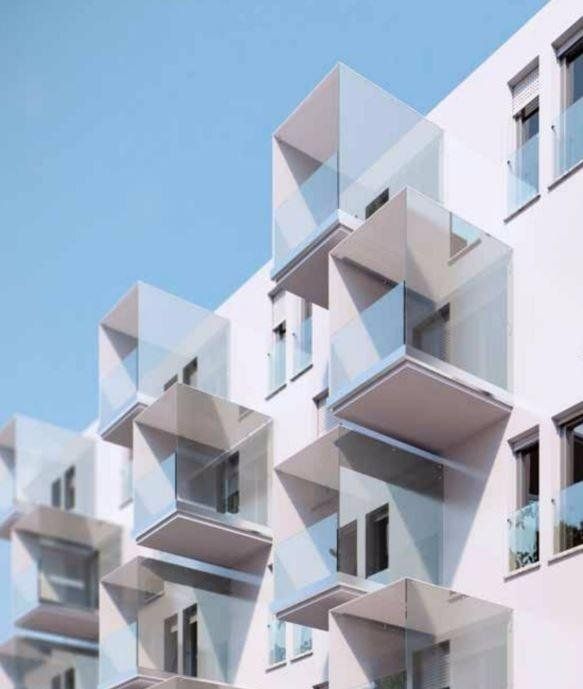 Moderno condominio con facciata bianca e balconi geometrici in vetro sullo sfondo di un cielo azzurro.