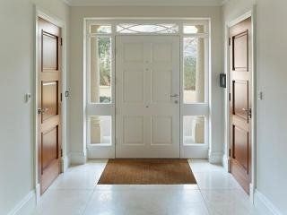 Luminoso atrio con doppie porte bianche, finestre laterali, porte laterali in legno e zerbino marrone.