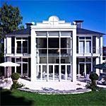 Moderna villa bianca con alte finestre di vetro, tetto blu e prato antistante curato sotto un cielo limpido