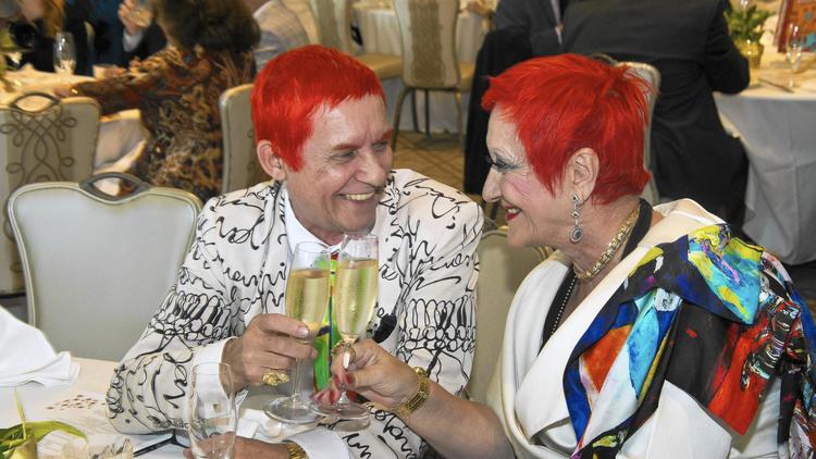 Man and Woman both wearing bright orange wigs smiling and toasting.