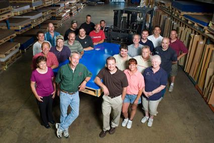Group of factory workers standing around a blue platform. Warehouse setting.