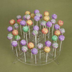 Cake pops on a clear, tiered display. Purple, orange, green, and yellow pops with sprinkles.
