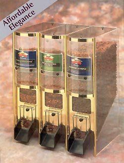 Three clear, gold-framed spice dispensers with clear containers holding various herbs, dispensing into black chutes.
