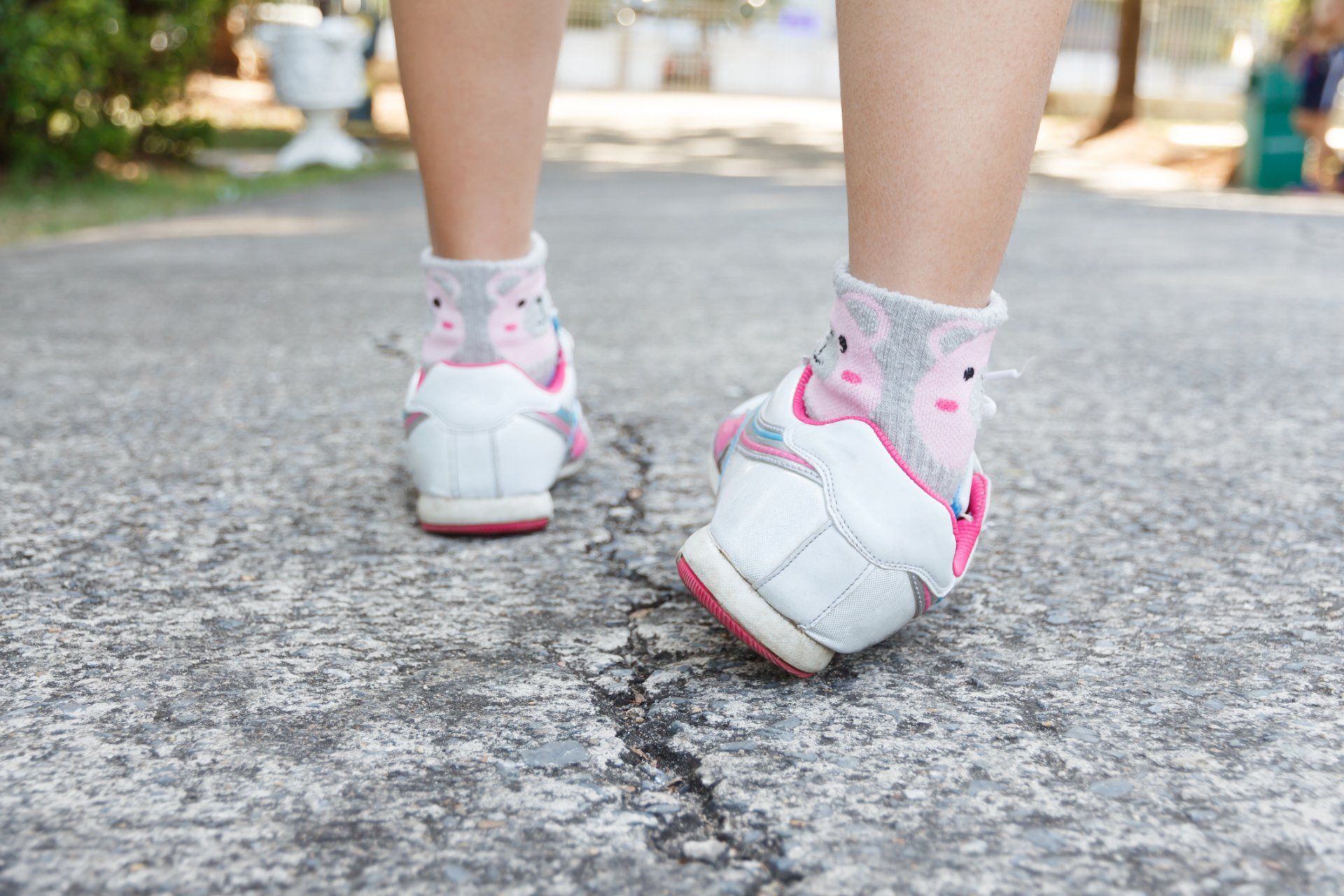 Person wearing white and pink shoes walking on a paved path outdoors