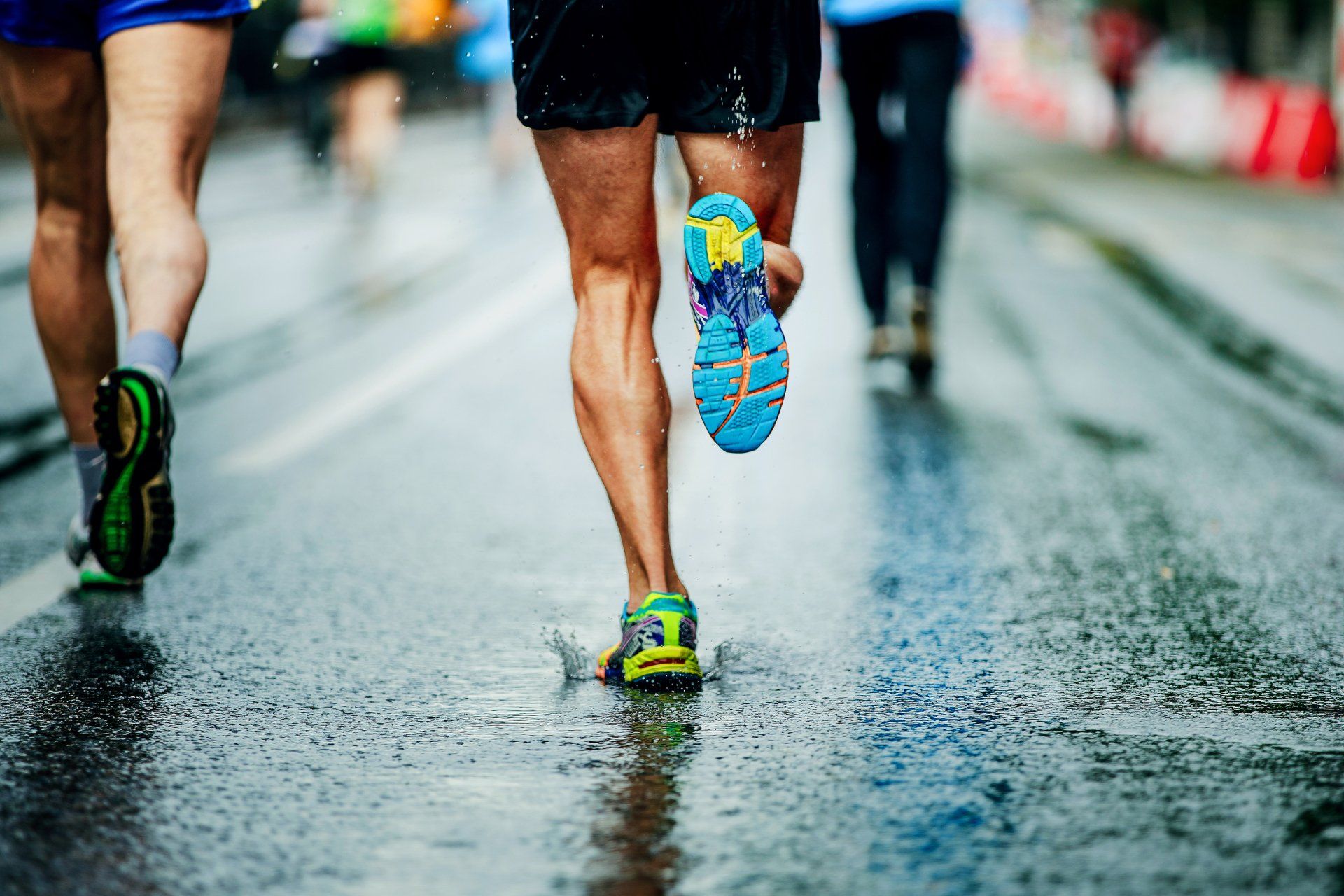 Runners’ legs on a wet road, with colorful shoes splashing during a race