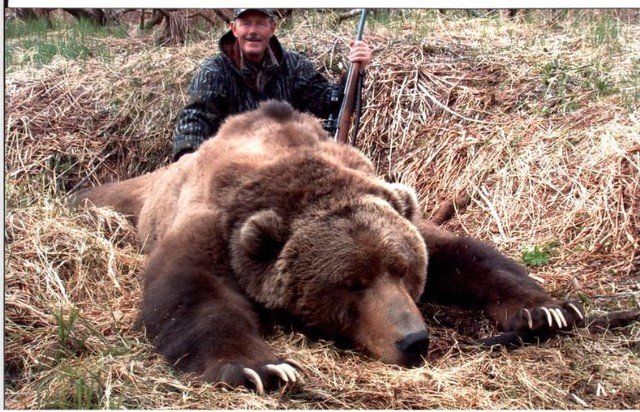 A man is standing next to a large brown bear.
