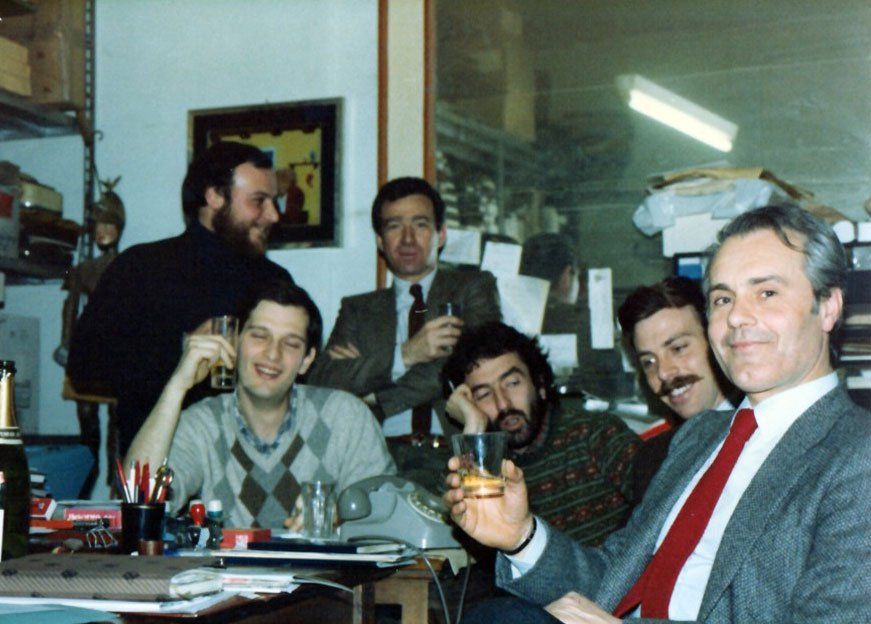 Un gruppo di uomini seduti attorno a un tavolo con un uomo che tiene in mano un bicchiere di whisky