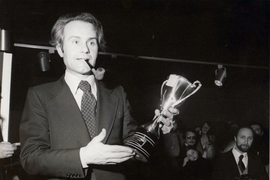 Un uomo con una pipa in bocca tiene in mano un trofeo