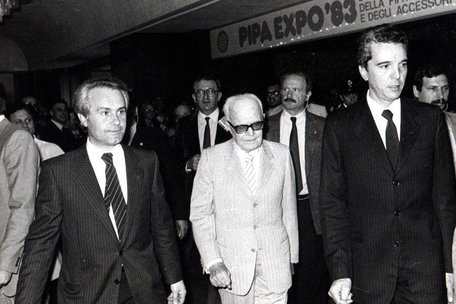 Un gruppo di uomini cammina davanti a un cartello che dice pipa expo 83
