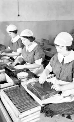 Una foto in bianco e nero di tre donne che lavorano in una fabbrica.