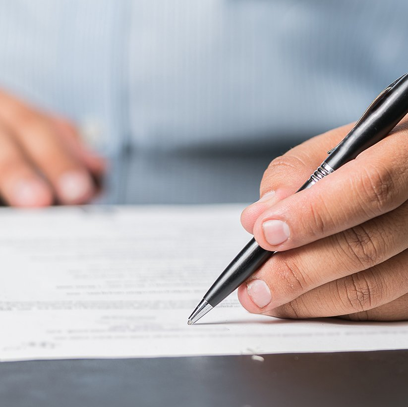 A close-up view of a hand using a black pen to sign a document on a desk.