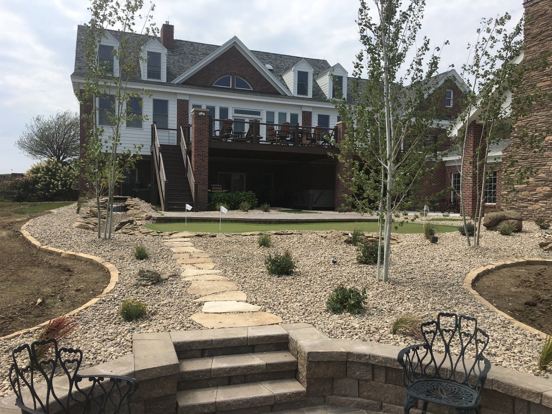 A large white house with a deck and landscaping, including stone path and gravel beds.
