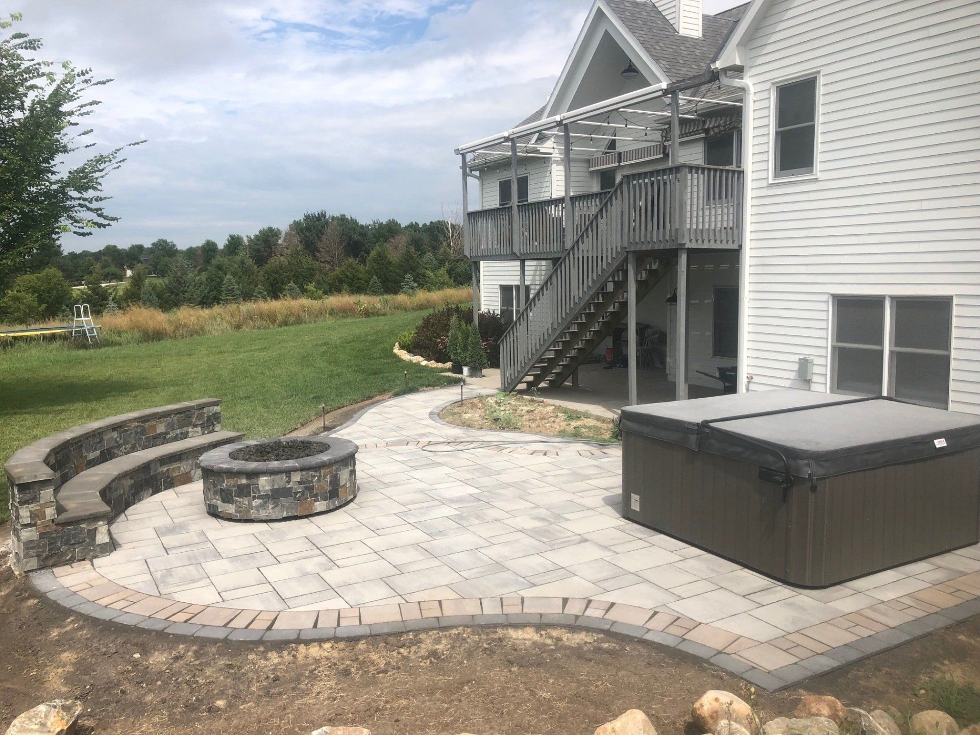 A patio with a fire pit and a hot tub in front of a house.