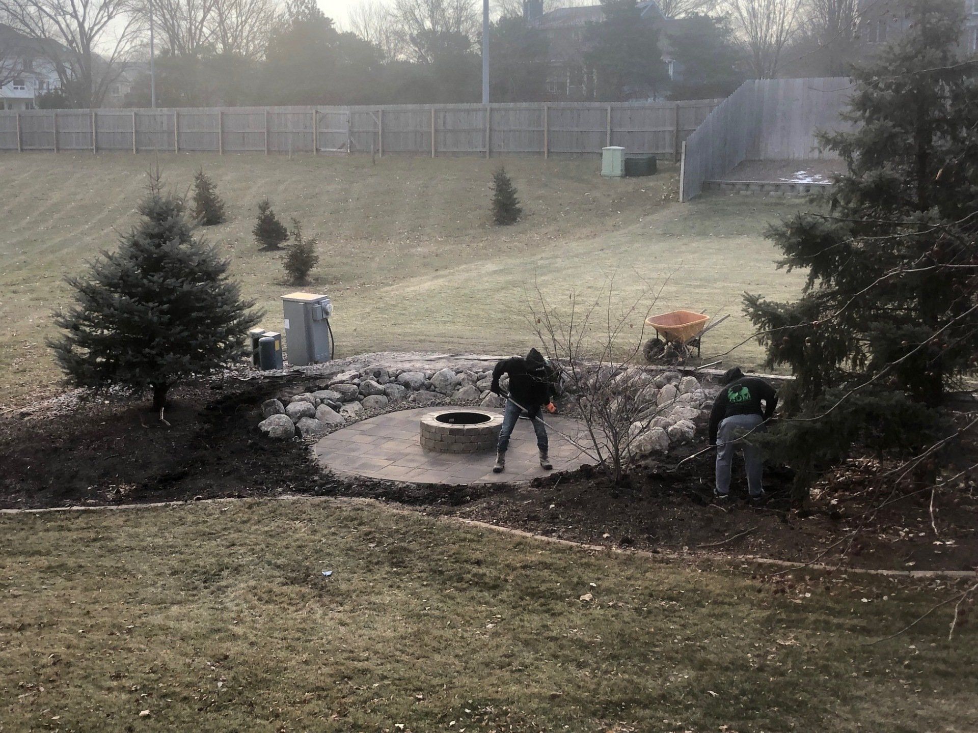 A man is standing next to a fire pit in a backyard.