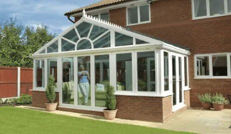 A large conservatory with a lady inside, looking out of the window