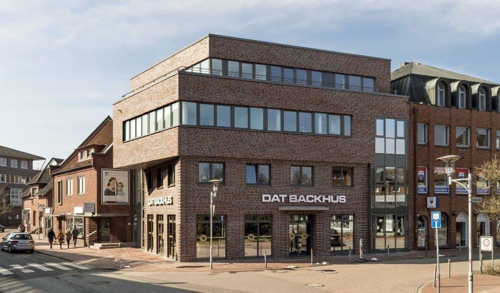 Moderne Backsteinfassade an einer sonnigen Straßenecke mit großen Fenstern und einem gut sichtbaren Ladenschild.
