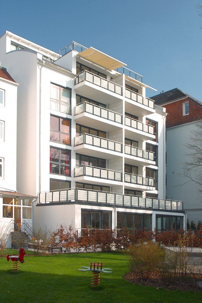 Modernes weißes Apartmentgebäude mit Balkonen neben einer grünen Rasenfläche unter klarem blauen Himmel