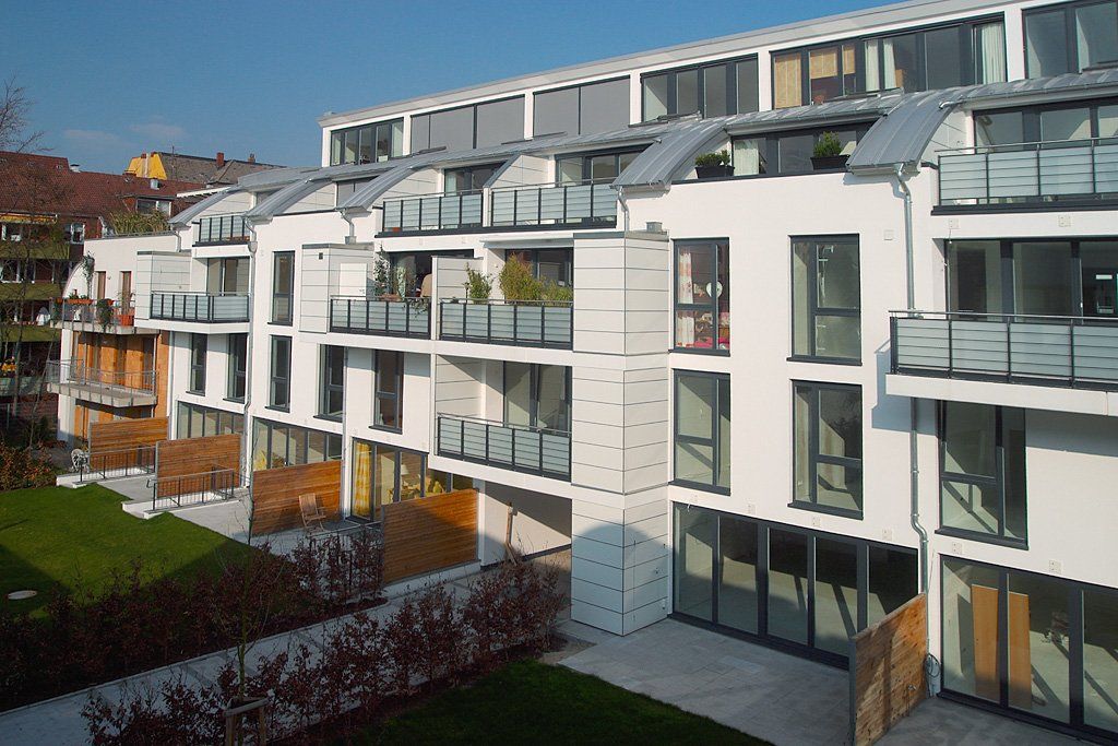 Moderne, weiße Apartmentgebäude mit Balkonen und großen Fenstern in einem begrünten Innenhof