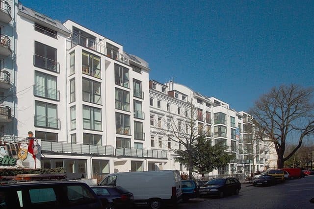 Weiße Wohnhäuser säumen eine ruhige Straße mit geparkten Autos unter einem klaren blauen Himmel