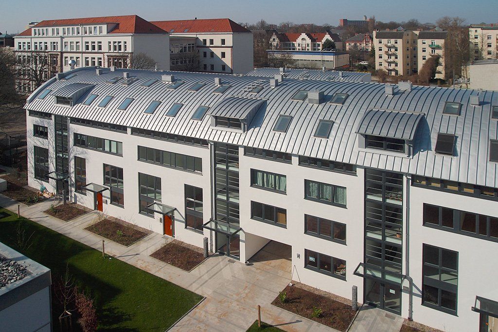 Luftaufnahme eines modernen weißen Gebäudes mit geschwungenem Metalldach und umlaufendem Innenhof.