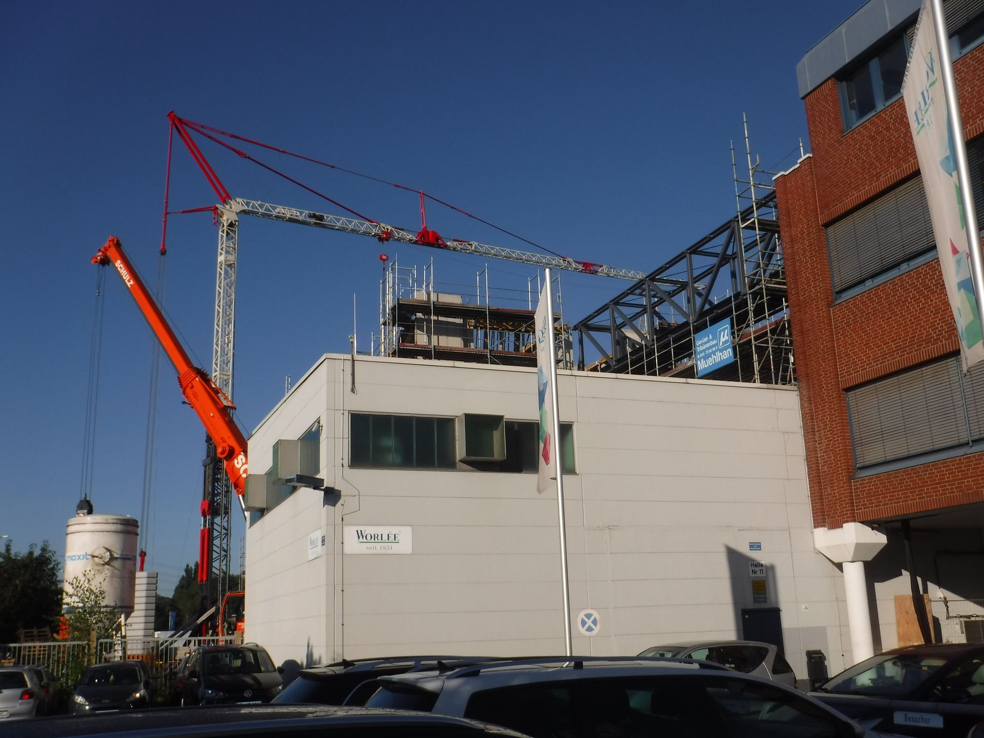 Baustelle mit Kränen neben einem großen weißen Gebäude und einem Backsteinbau unter klarem blauen Himmel