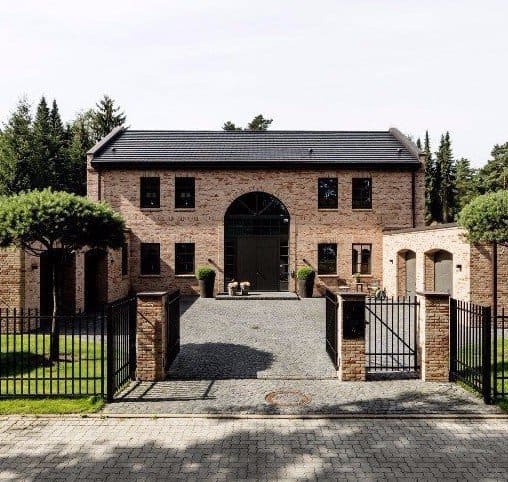 Backsteingebäude mit Bogeneingang, schmiedeeisernen Toren, Kiesauffahrt und Bäumen davor