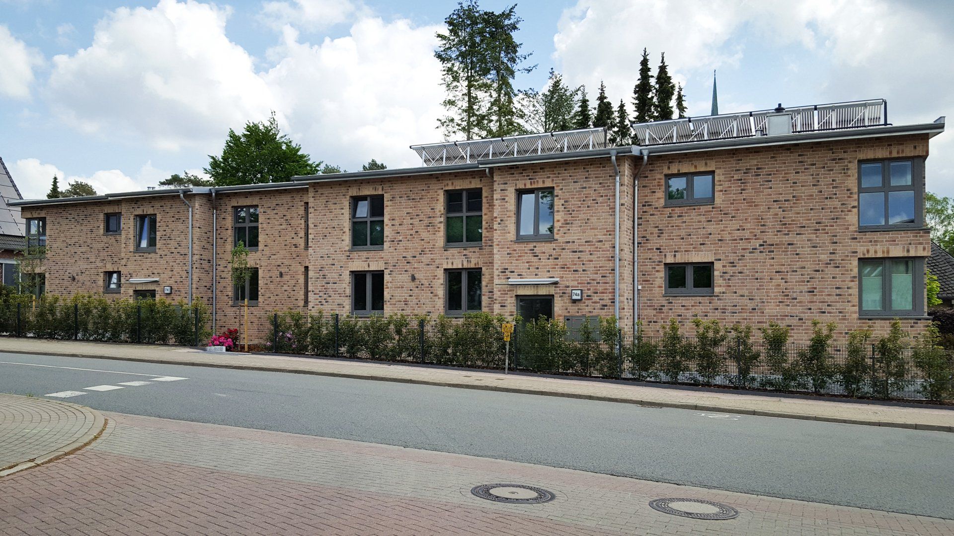 Modernes Backstein-Mehrfamilienhaus an einer ruhigen Straße mit Bäumen und bewölktem Himmel