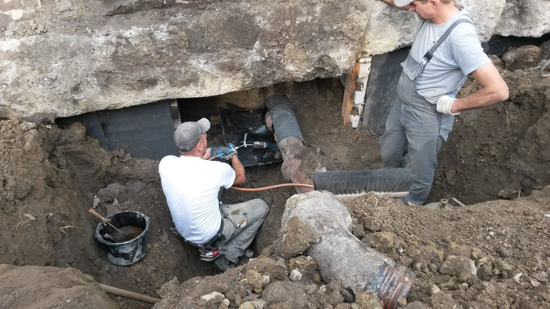 Zwei Arbeiter graben sich in eine Felswand neben einer kleinen unterirdischen Öffnung.