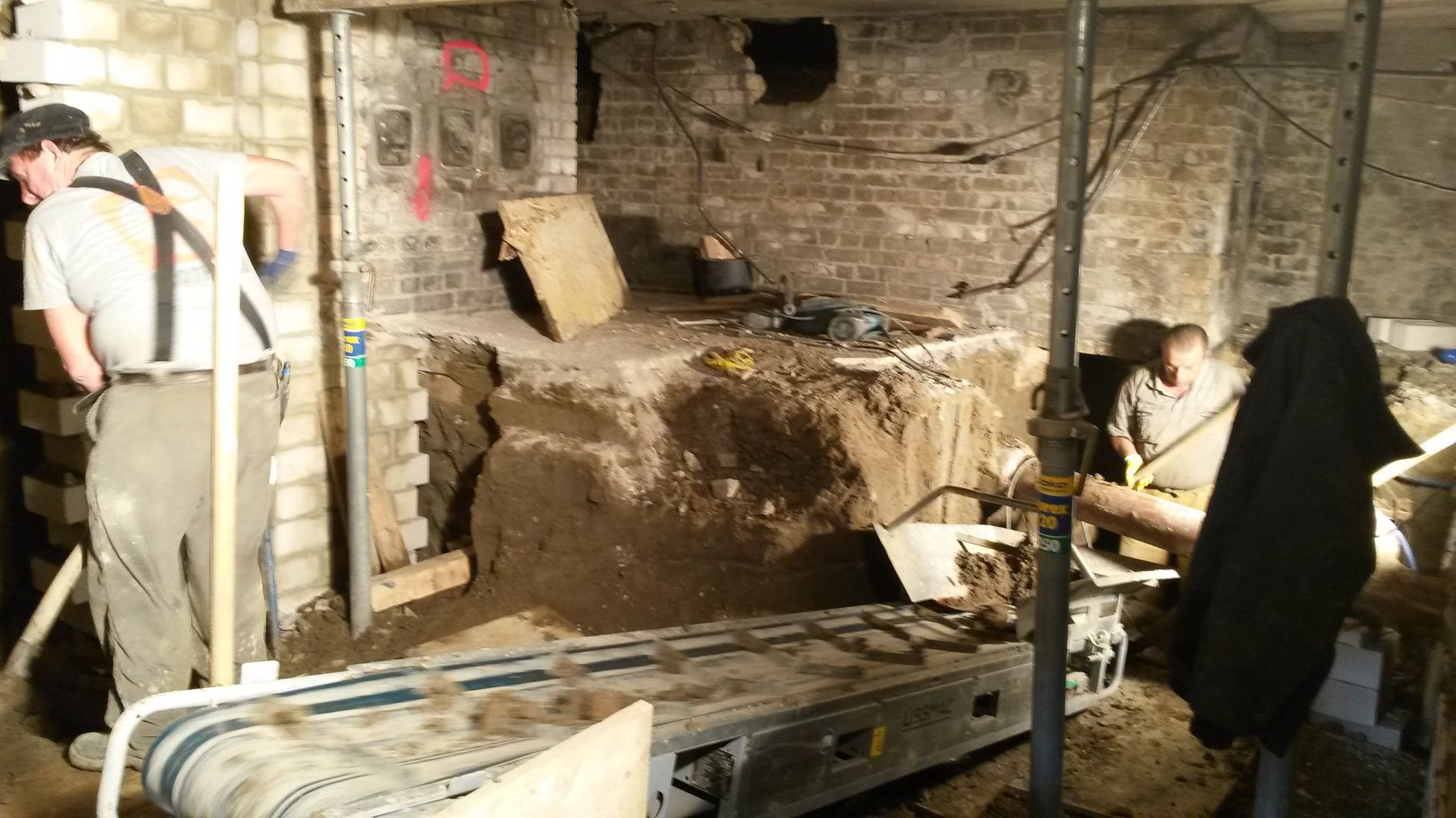 Archäologen graben in einer dunklen Kammer eine mit Ziegeln ausgekleidete Ausgrabungsstätte mit Werkzeugen und Kabeln aus.